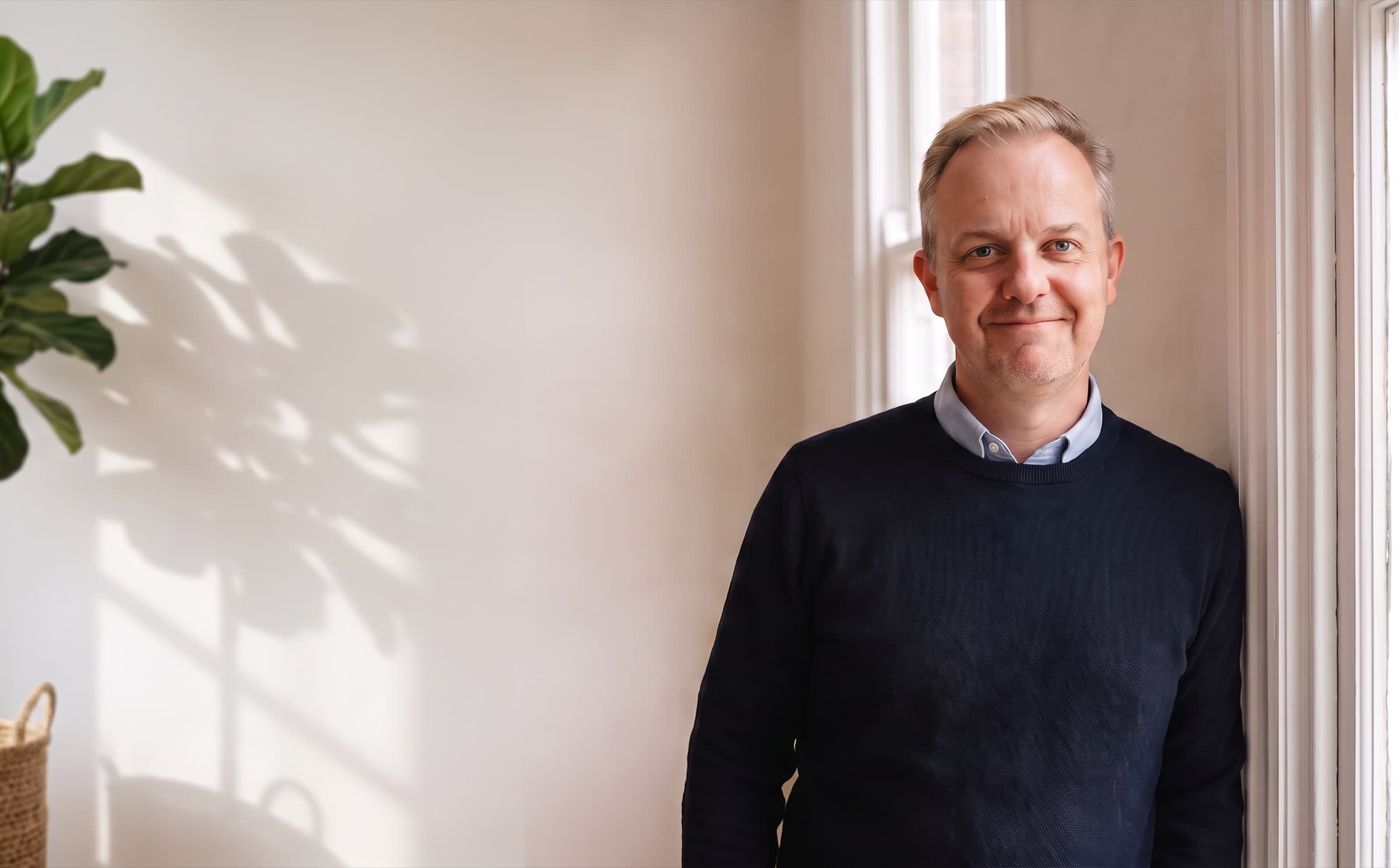 Mark Craig standing by a window in his counselling room, smiling.
