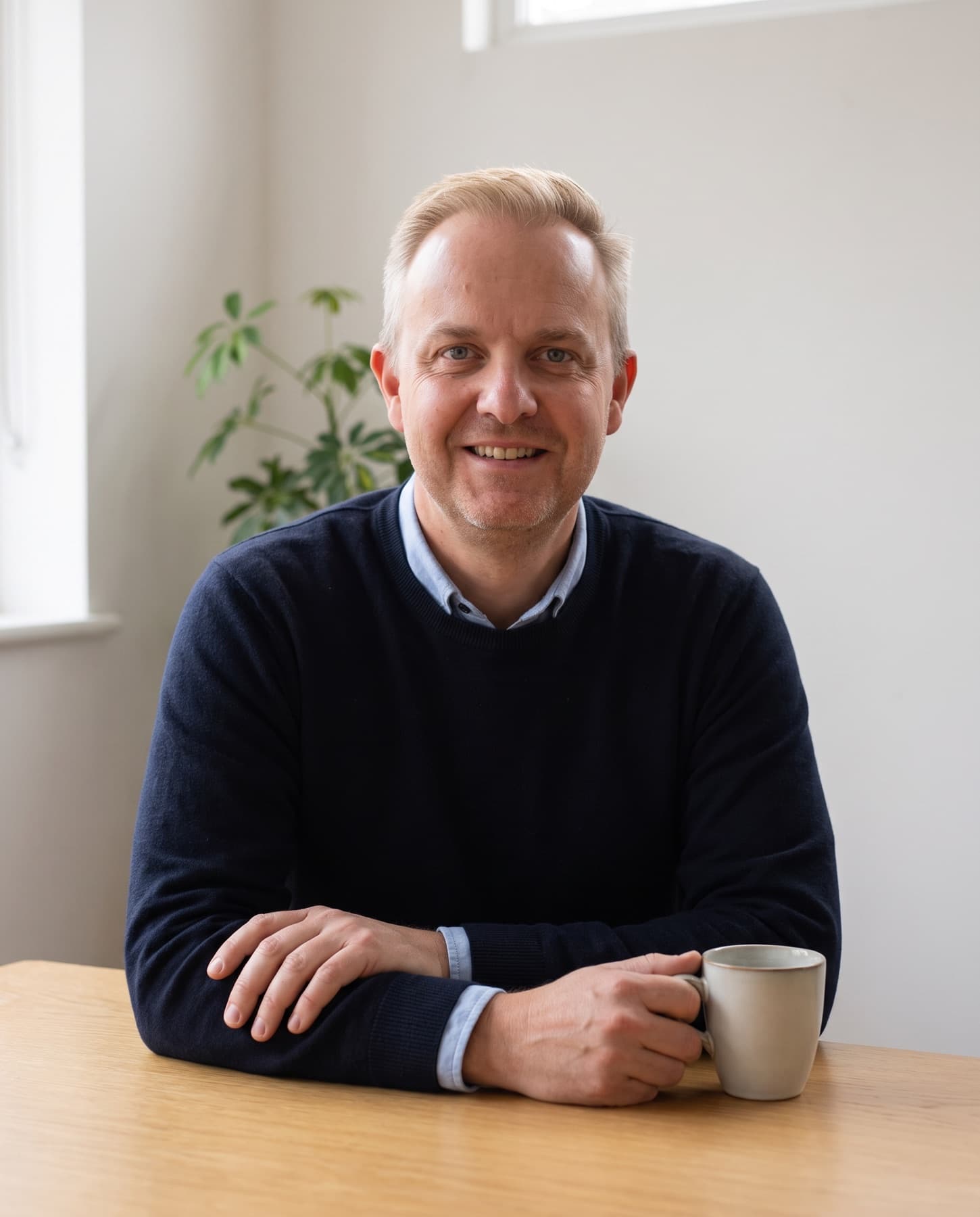 Mark Craig sitting at a table with a mug of tea, smiling.